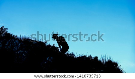 Dramatic silhouette of a person hiking and climbing a steep mountain Royalty-Free Stock Photo #1410735713