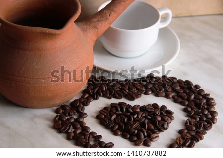brown clay Turk for cooking Arabic Turkish coffee, white clean Cup and saucer and roasted coffee beans in the shape of a heart, selective focus