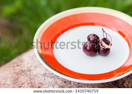 wedding rings and cherries. The concept of a wedding. Golden rings close up with cherry berries like background. Empty space for text. Invitation card.two rings on plate with berries