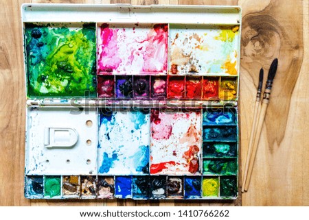 Watercolor in palette with blobs of paint and a brush. Vintage stylized photo with wooden texture background. Copy space for add text or art work designs.