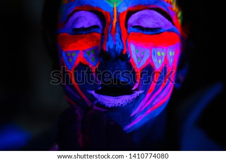 Ultraviolet black light glowing bodyart processing on young woman's face. Pink and purple dyes in cold blue light