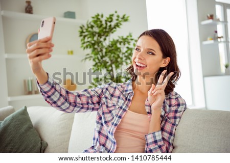 Close up photo of cute positive cheerful satisfied content make photos v-signs laughter laugh wavy greet friends students curly haircut hairstyle checked shirt outfit sit divan enjoy apartment