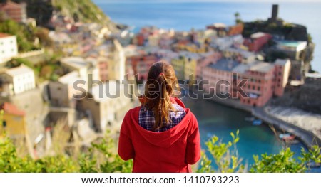 Young female tourist enjoying the view of Vernazza, one of the five centuries-old villages of Cinque Terre, located on rugged northwest coast of Italian Riviera, Liguria, Italy. Traveling off season.