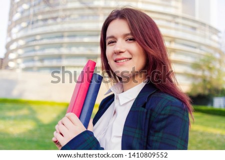Smiling portrait of female university student outdoors on Campus holding books looking to camera. Confident student holding books 