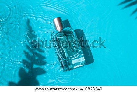 Transparent glass cosmetic perfume bottle in the blue water under shadows of tropical leaves. Top view Royalty-Free Stock Photo #1410823340