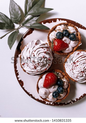 Delicious berry tartlets with meringue on a white vintage plate. Sweet treat on white background. Flat lay. Top view