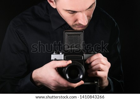 Man photographer holding a camera. Shooting process. Retro photo camera medium format on a black background. Horizontally framed shot.