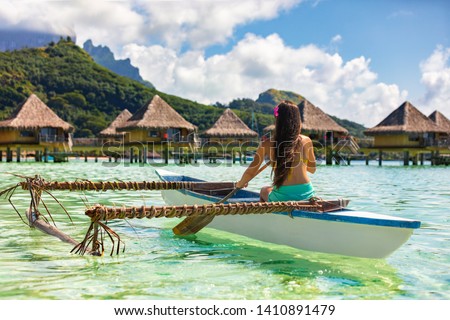Outrigger Canoe - woman paddling in traditional French Polynesian Outrigger Canoe for recreational activity and watersport competition. Bora Bora with  overwater bungalow resort hotel sport lifestyle  Royalty-Free Stock Photo #1410891479