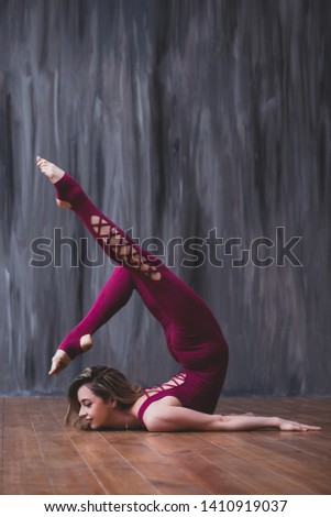 Yoga scorpion pose. Fit sporty girl is stretching. Young beautiful gymnast woman in a jumpsuit doing gymnastic exercises