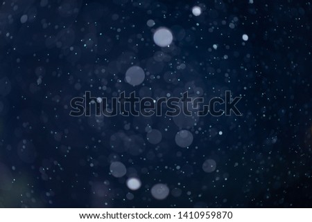 Abstract falling snow or rain bokeh texture overlay on blue background.