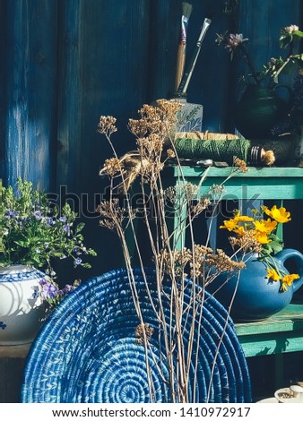Blue wicker round dish, wild yellow flowers in pot, vase, wooden background. Still life in rustic style, daylight, harsh shadows. Beauty, Nature, Countryside lifestyle, weekend, vacation, art concept