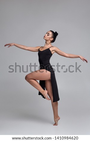 Dancing ballerina in a black dress. Contemporary graceful performance on a gray background.