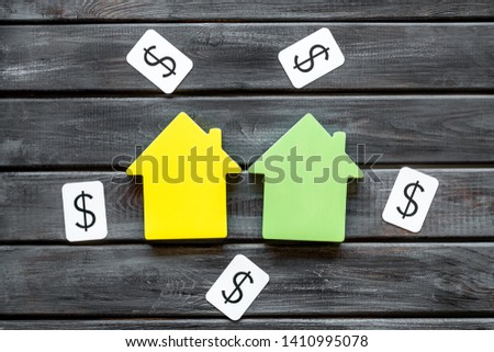 Buy house with house figure and dollar signs on office desk wooden background top view