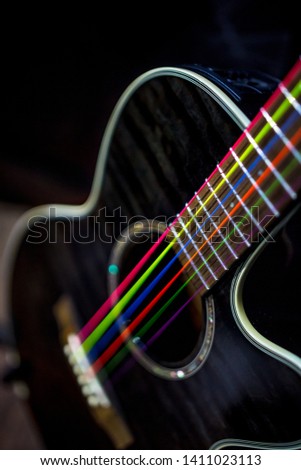 electric acoustic unplugged black guitar with colorful rainbow strings dark background