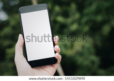 Cropped hand, Close-up of male hand holding Mobile Phone with blank screen for your text message or content, man's hand using cellphone with empty display in green city, bokeh light, Mockup image.