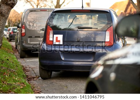 Blue hatchback car with a learner driver sign at the rear, parking at the side of the road, parking training, parallel parking