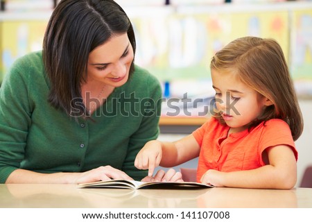Elementary Pupil Reading With Teacher In Classroom Royalty-Free Stock Photo #141107008