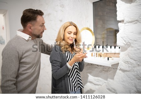 Attractive fragrance. Gorgeous smiling woman testing a perfume on a blotter being with her husband in a perfumery.