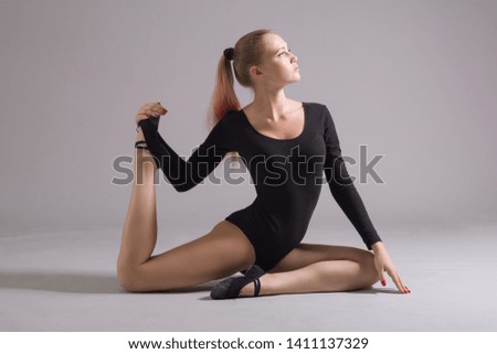 Female gymnast performs gymnastic exercises on a gray background.