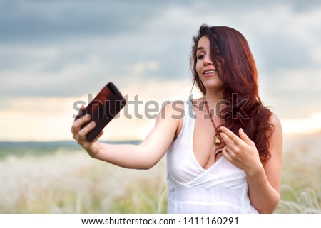 beautiful woman with a mobile phone in nature makes photo of herself