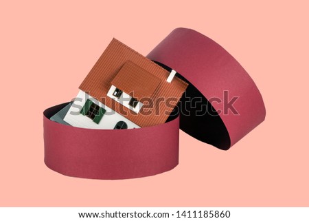 Model of house and round red gift box on the light coral background. House painted white under the tiled roof.