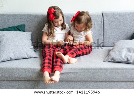 Two little girls sitting on sofa and playing on smartphone. sisters have fun with a mobile phone, watch a children's movie or cartoon. Technology of the new generation are addicted to gadgets concept