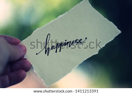 People hand holding pice of paper with word "Happiness"