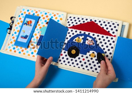 CHILDREN'S LEARNING DEVELOPING BOOK, SEWING FROM A FABRIC. BOY HANDS GATHERING A CAR.