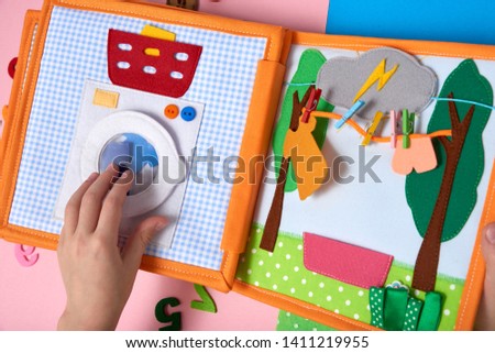 CHILDREN'S LEARNING DEVELOPING BOOK, SEWING FROM A FABRIC. CHILD PLAYS WITH HANDS WITH A BOOK.