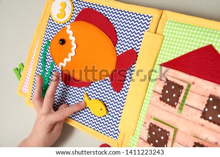 CHILDREN'S LEARNING DEVELOPING BOOK, SEWING FROM A FABRIC. CHILD PLAYS WITH HANDS WITH A BOOK.