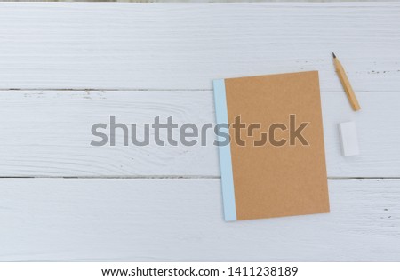 Flat lay of plain notebook with brown pencil and rubber on white background. Minimal and simple composition for wallpaper. Copy space for text. Education, idea and love photo concept.
