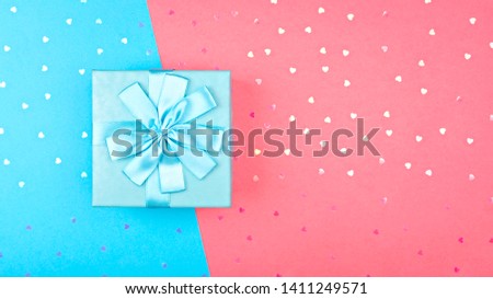 Holiday Banner. Blue box with a gift on a paper background of blue-pink color. With scattered holographic glitter in the shape of a heart. With copy space for your design.