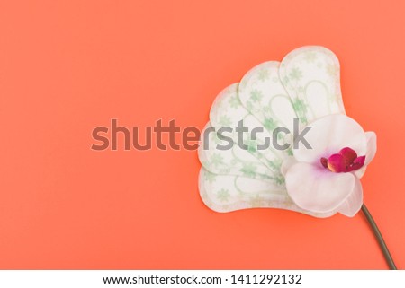 Sanitary napkins, Panty liners and orchid flower on coral background. Feminine hygiene products.