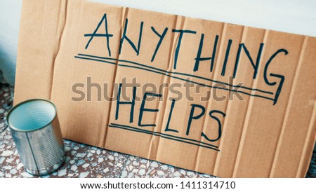 Fighting adversity. Homeless man with sign and money tin. Help, please. Poverty. "Anything helps" says beggar's cardboard sign.