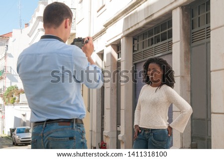 Man taking photo of smiling black woman outdoors. Man and woman walking in city. Man is standing back to camera. Tourism concept.