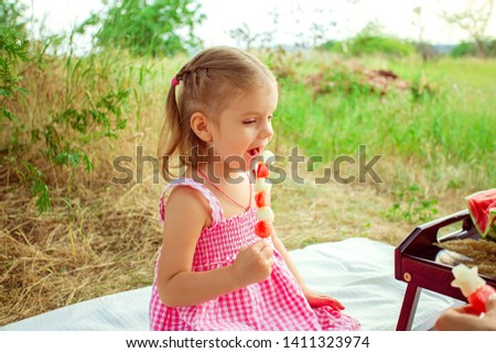 Funny portrait of an incredibly beautiful little girl eating watermelon, healthy fruit snack, adorable toddler child playing in a sunny meadow on a hot summer day.