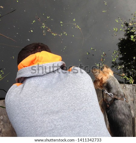 Macro photo of a man and a dog looking at the water. Man and dog view from the back. Friendship is a man and a dog looking at the river in nature on the pier.