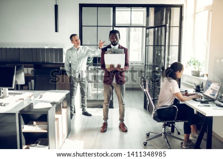 Firing trainee. Angry boss firing dark-skinned trainee holding his box with staff after monthly work
