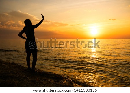 silhouette of a young girl. makes selfie at sea sunset.
