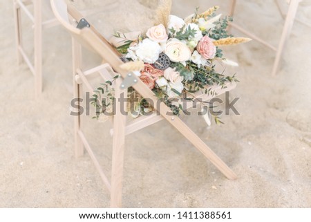 Bohemian wedding bouquets on wooden chair on sand by sea ​​coast
