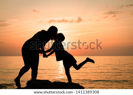 silhouettes of mom with daughter. mother and daughter kiss at sunset.
