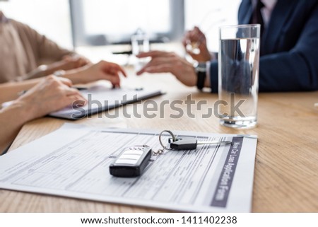 selective focus of car keys near agreement, glass of water, car dealer and customers 