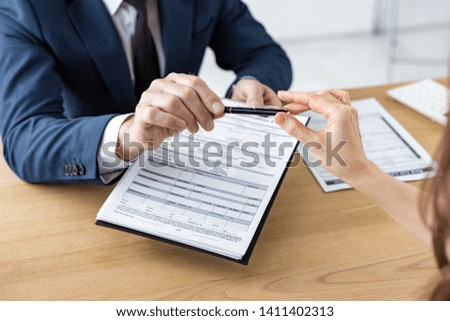 cropped view of car dealer giving pen to woman while holding clipboard with document 