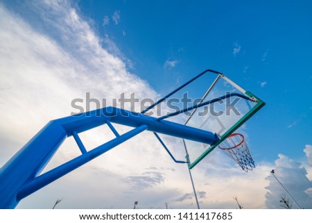 The basketball stands on the outdoor basketball court are under the blue sky and white clouds.