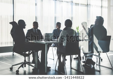 Silhouettes of people sitting at the table. A team of young businessmen working and communicating together in an office. Corporate businessteam and manager in a meeting. Royalty-Free Stock Photo #1411448822