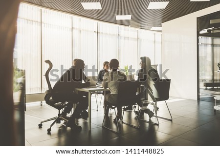 Silhouettes of people sitting at the table. A team of young businessmen working and communicating together in an office. Corporate businessteam and manager in a meeting. Royalty-Free Stock Photo #1411448825