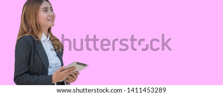 
Smiling young pretty Asian business woman with tablet computer looking up on sky on sky, studio shot isolated on pink banner background with copy space.