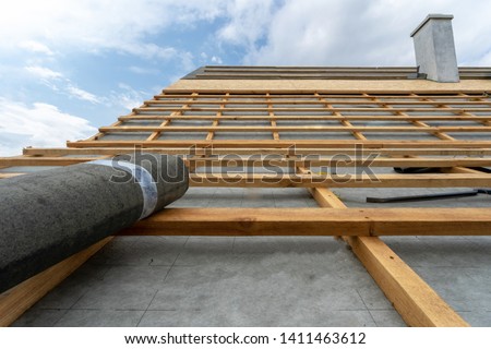 Concept of residential building under construction. Vertical photo of unfinished wooden roof top with special waterproof bitumen membrane of new modern house