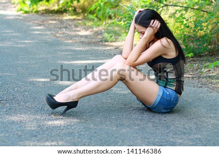 Sad girl sitting down on road hiding her head on her hands