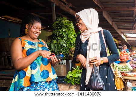 African lady selling vegetables and tomatoes in a local market swiping a customer's credit card in her pos Royalty-Free Stock Photo #1411480076